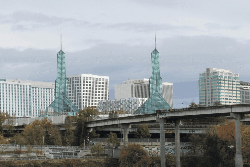 Portland, Oregon skyline featuring the glass-spired Oregon Convention Center towers, downtown buildings, and an elevated highway bridge in the foreground.