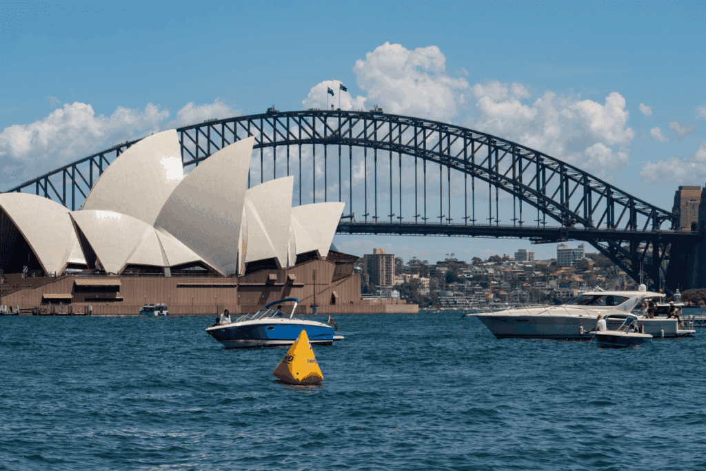 Sydney Opera House and Harbour Bridge viewed across the water, with boats and a yellow marker buoy in the foreground