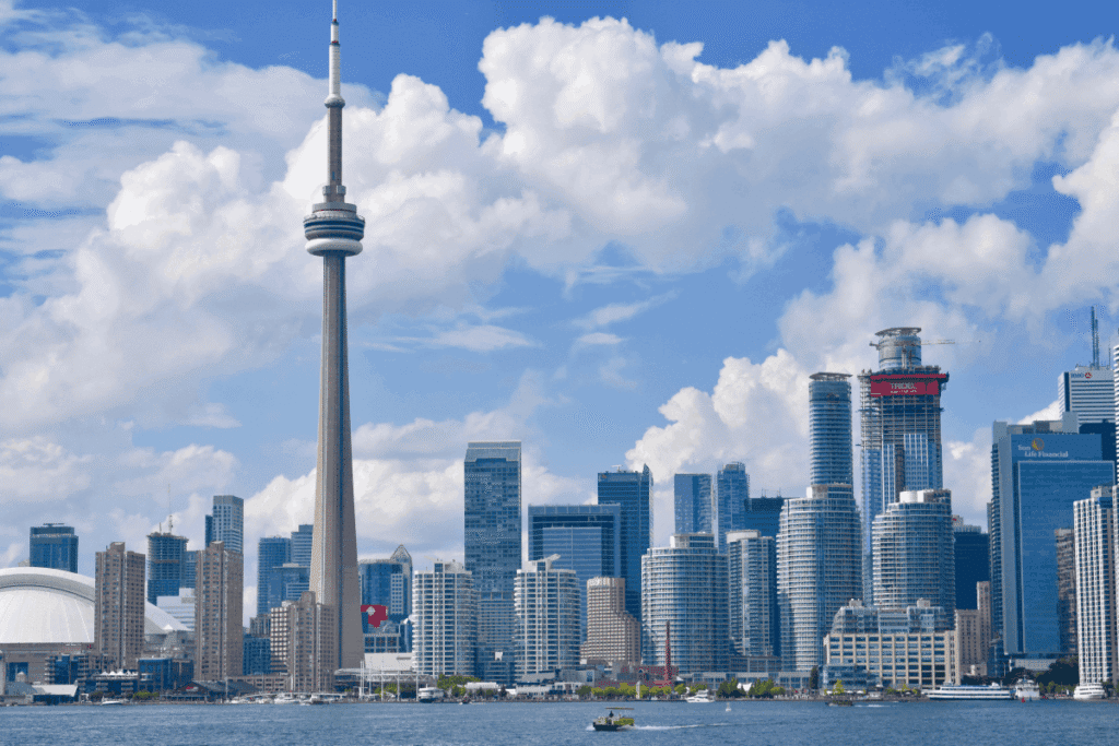 Toronto, Canada skyline viewed from the water, featuring the CN Tower rising above downtown skyscrapers under a partly cloudy sky.