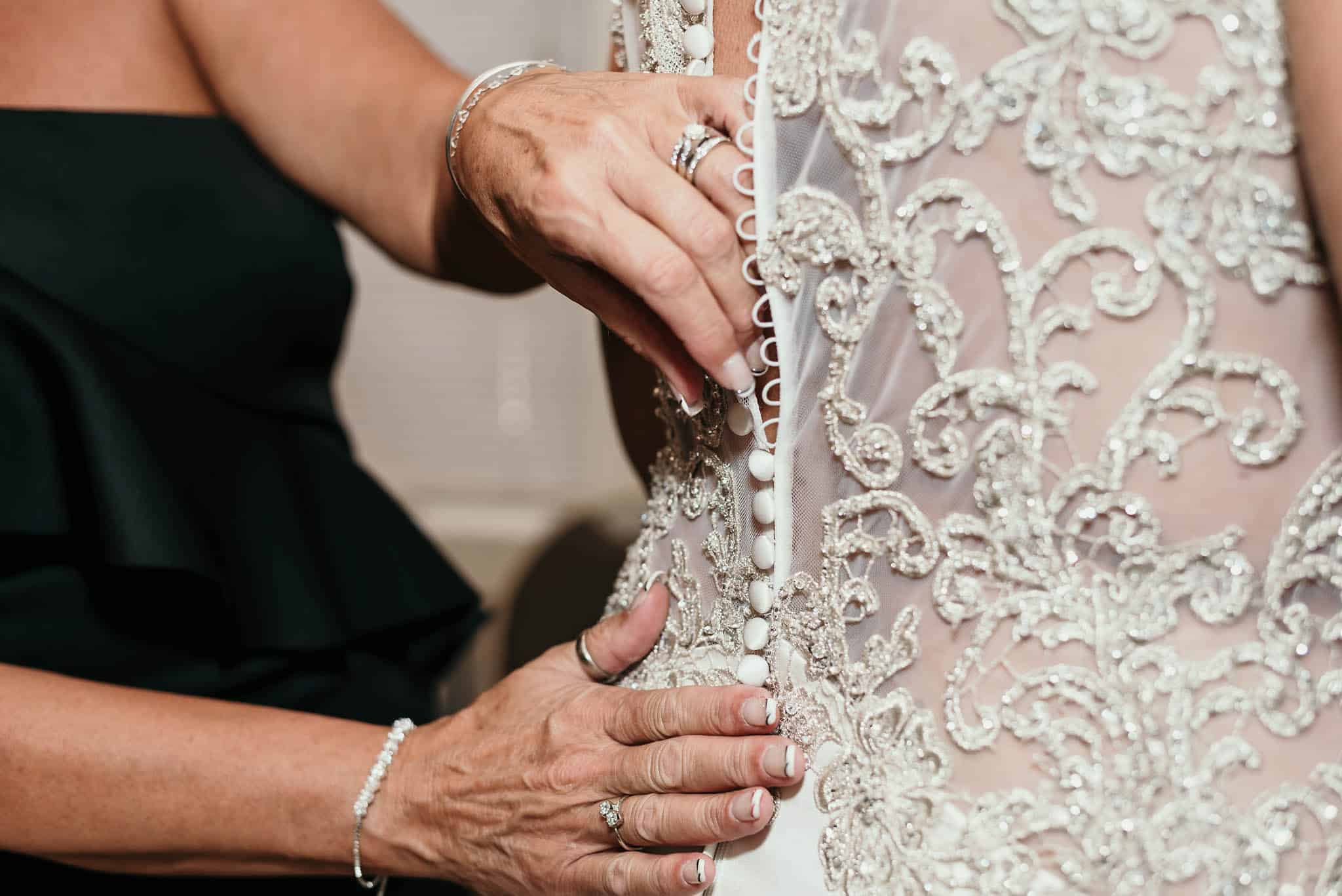 close up of mother of the bride's hands fastening the loops around buttons of wedding gown