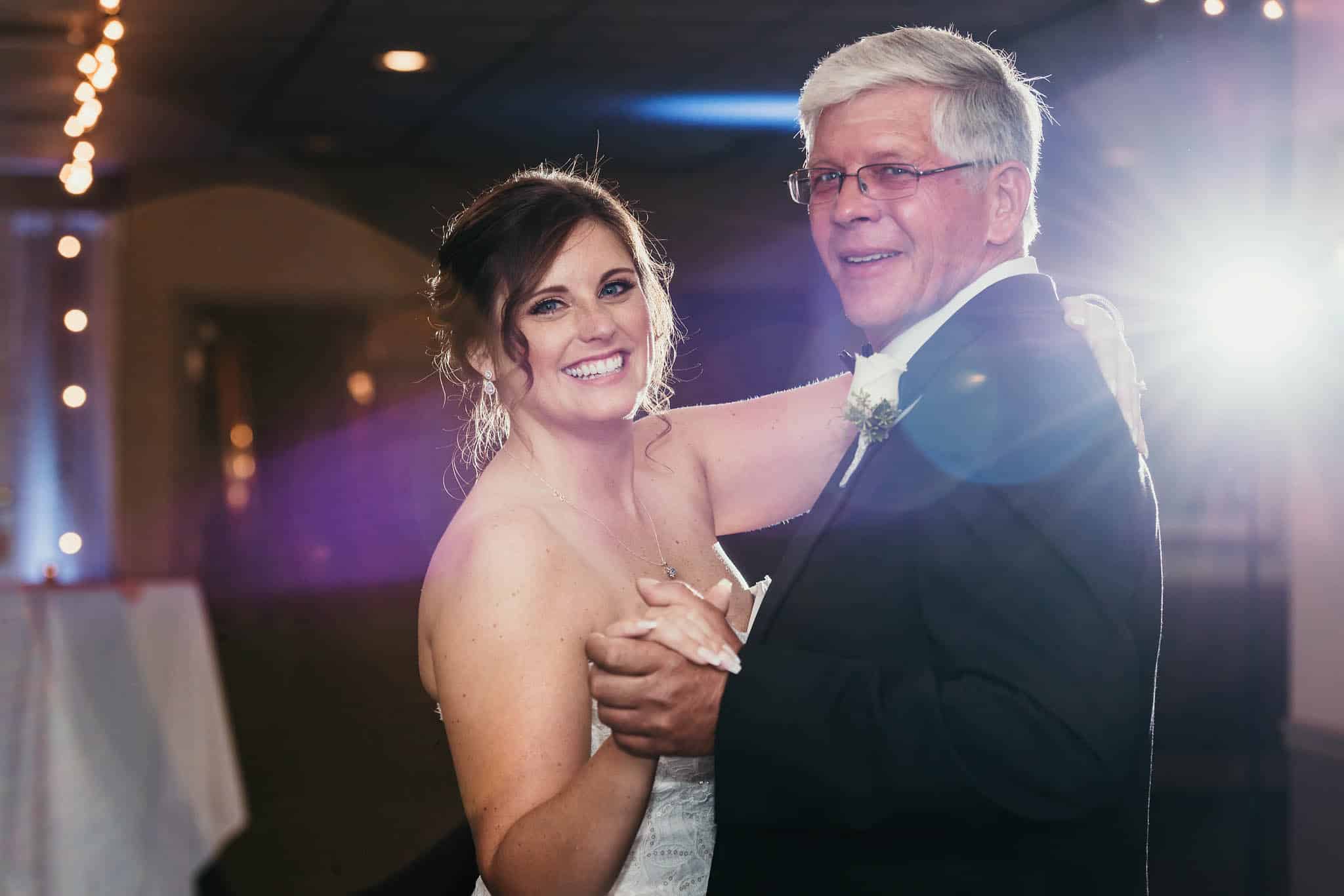 Bride and father smile at the camera during father-daughter dance at intimate country club wedding
