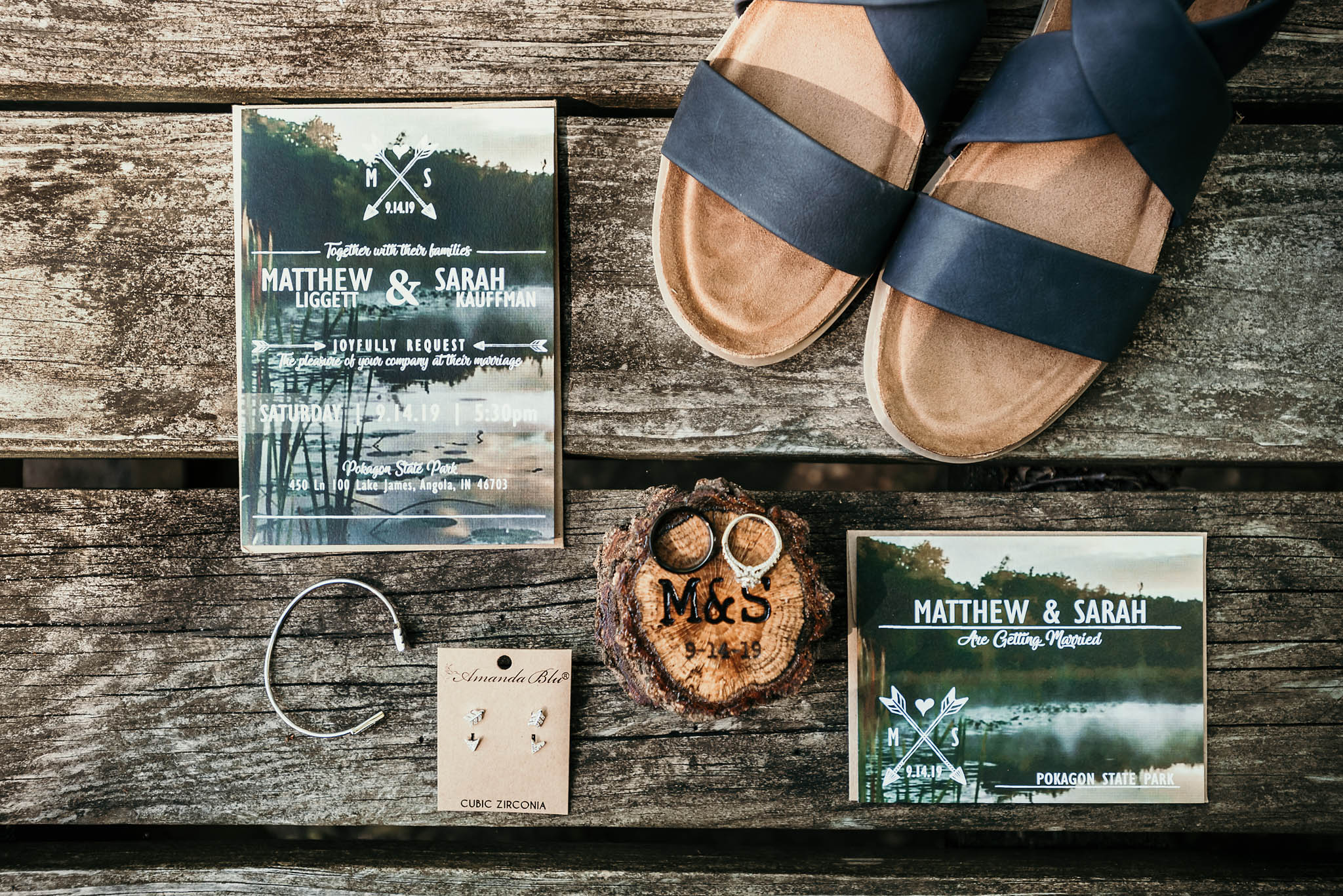 Details of wedding invitation, jewelry, bridal shoes, and wedding rings on picnic table at Pokagon State Park unique outdoor DIY wedding