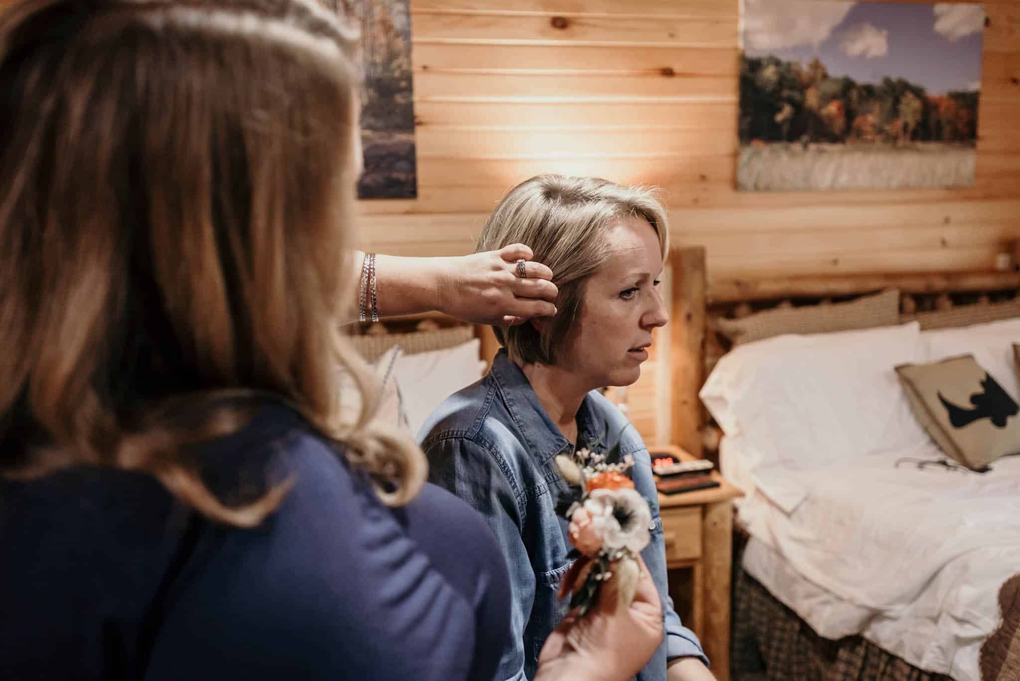 Bridesmaid putting floral hairpiece in blonde bride's hair during bridal prep