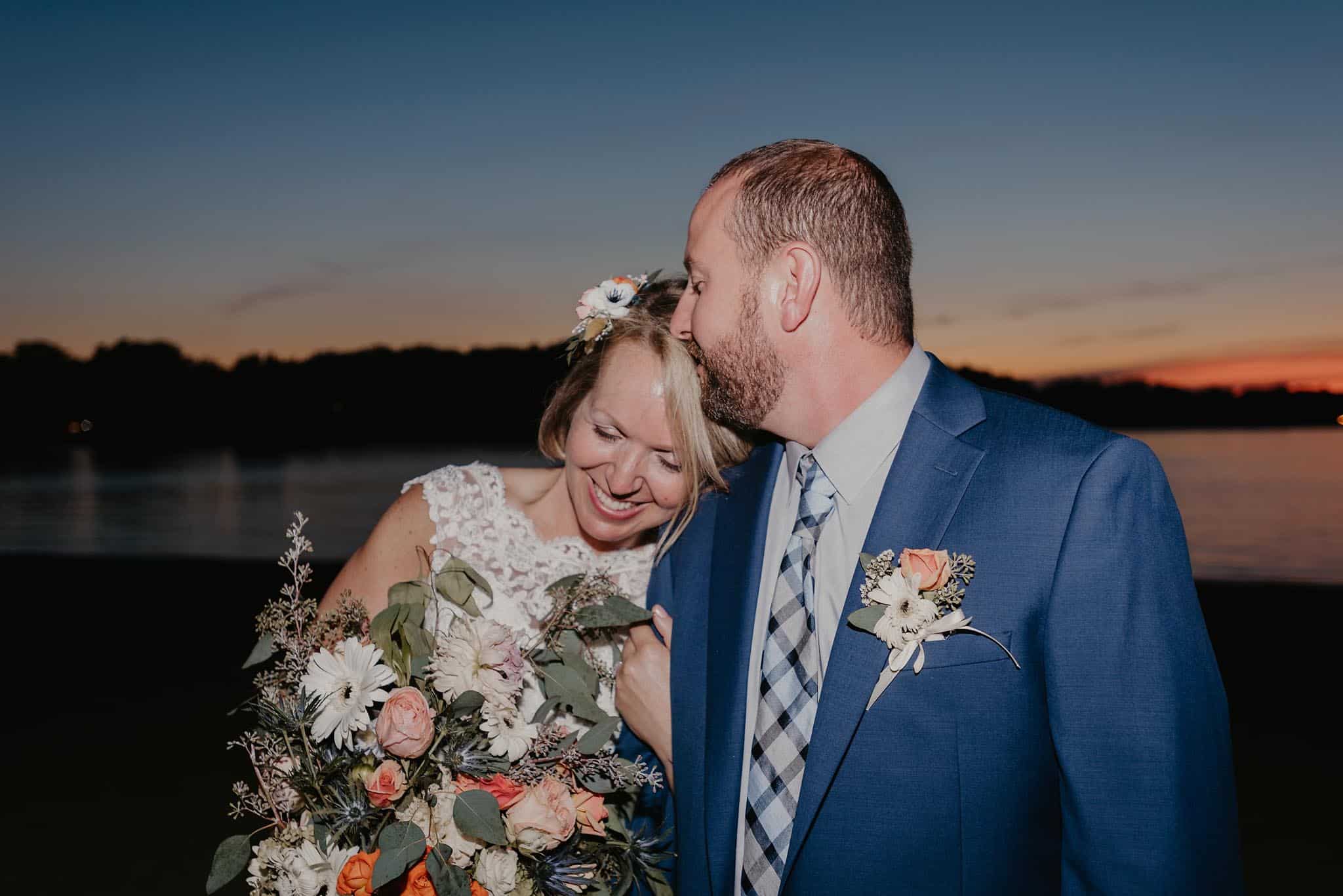 Groom kissing bride's forehead on beach at sunset at Pokagon State Park