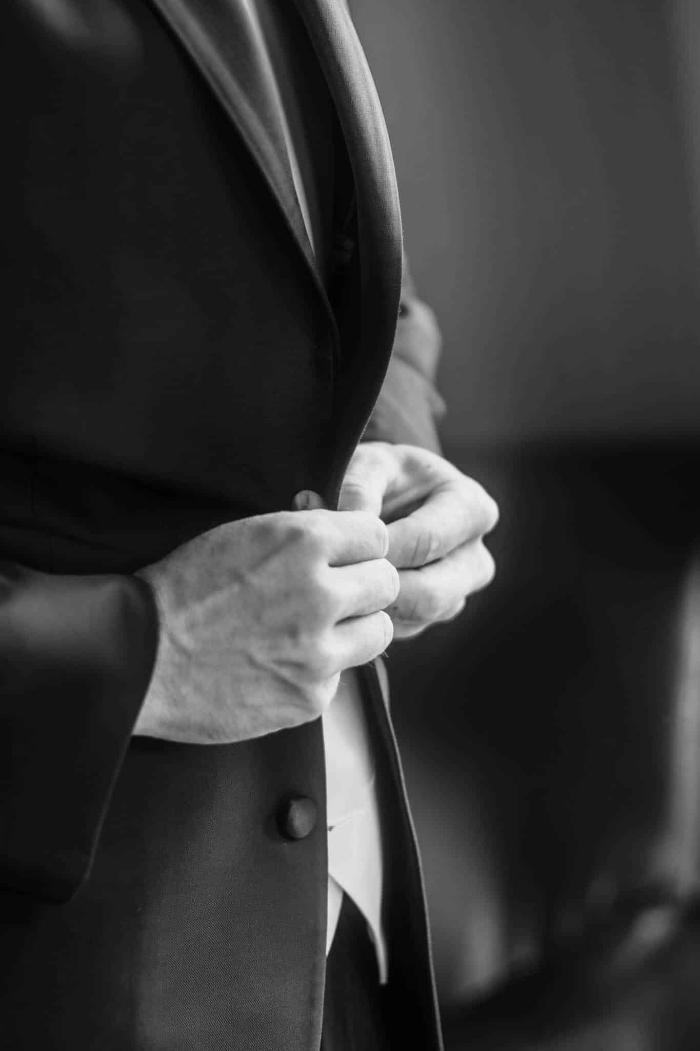 Black and white close up of groom buttoning suit