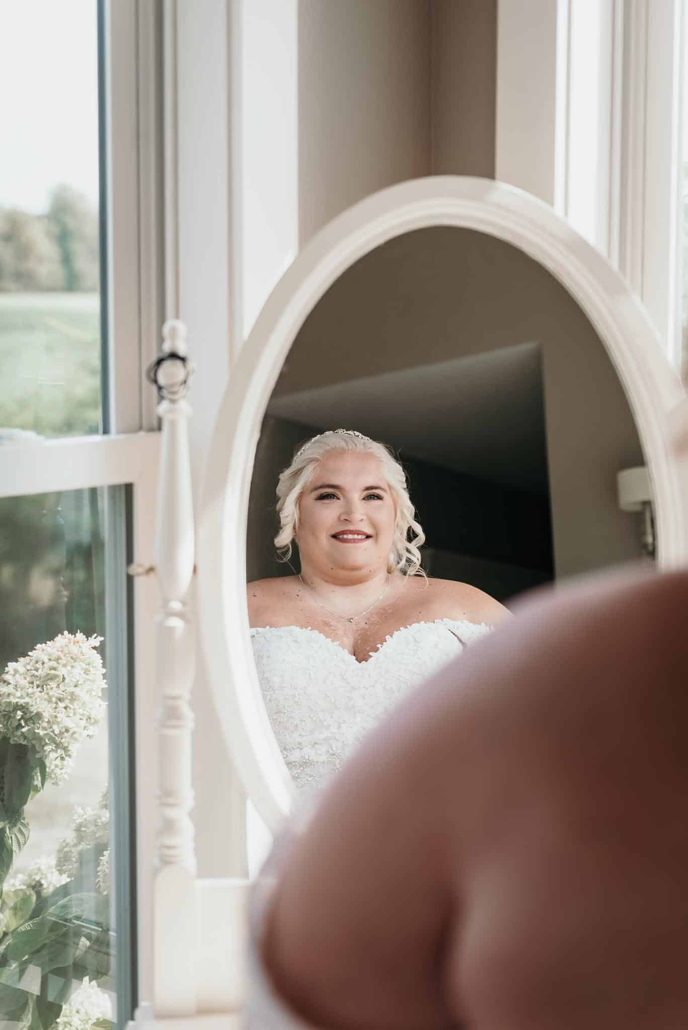Bride looking at herself in mirror after getting dressed during bridal prep