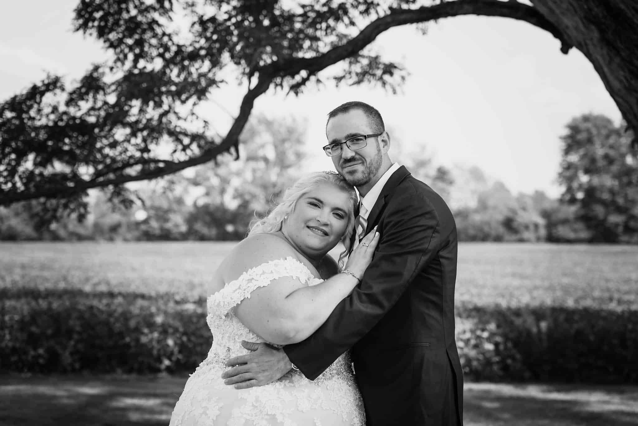 Black and white photo of bride and groom posing in front of field outside