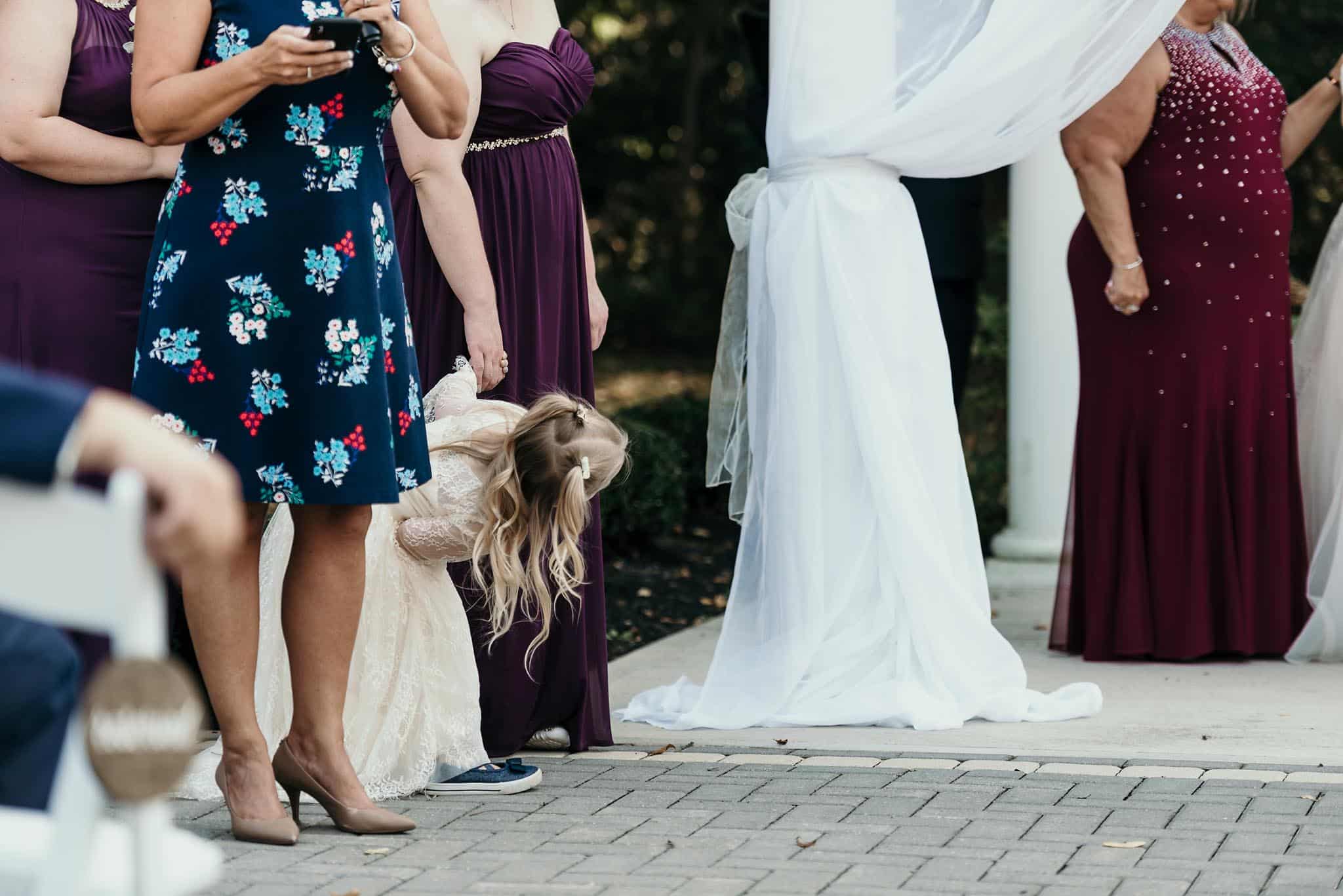 Flower girl peeking around maid of honor to see bride and groom