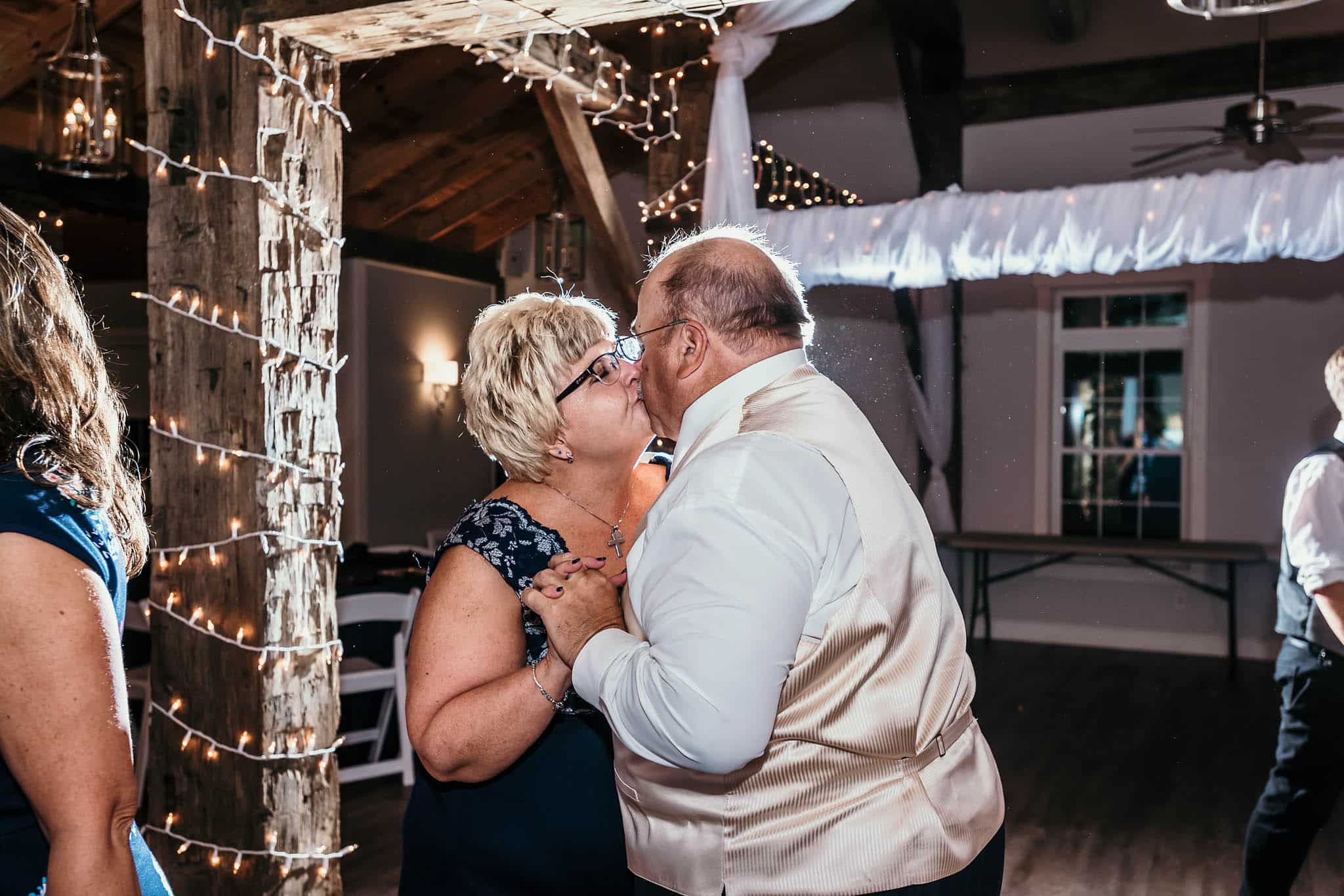 Mother and father of groom dancing and kissing during reception of intimate fall wedding at the Lodge at River Valley in Yorktown, Indiana