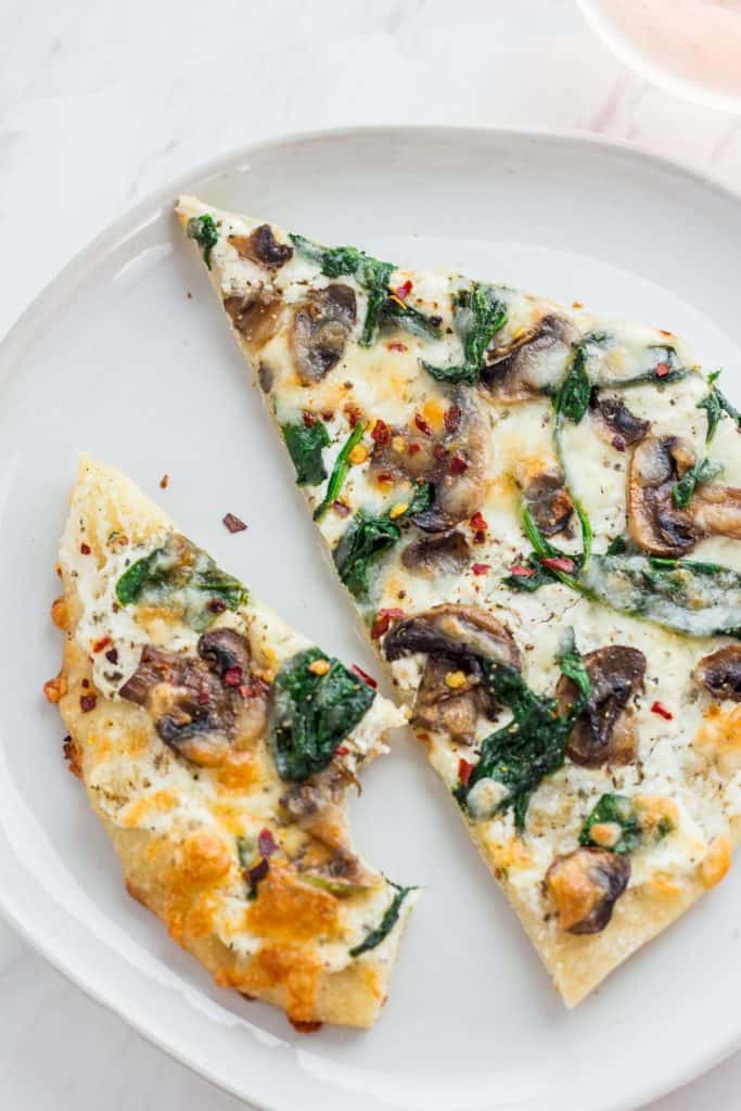 Two slices of white pizza on a white plate with the glass of rose in the background