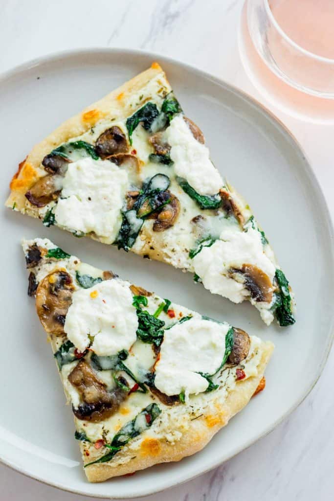Two slices of white pizza with dollops of extra ricotta cheese on top. Glass of rose in the background.