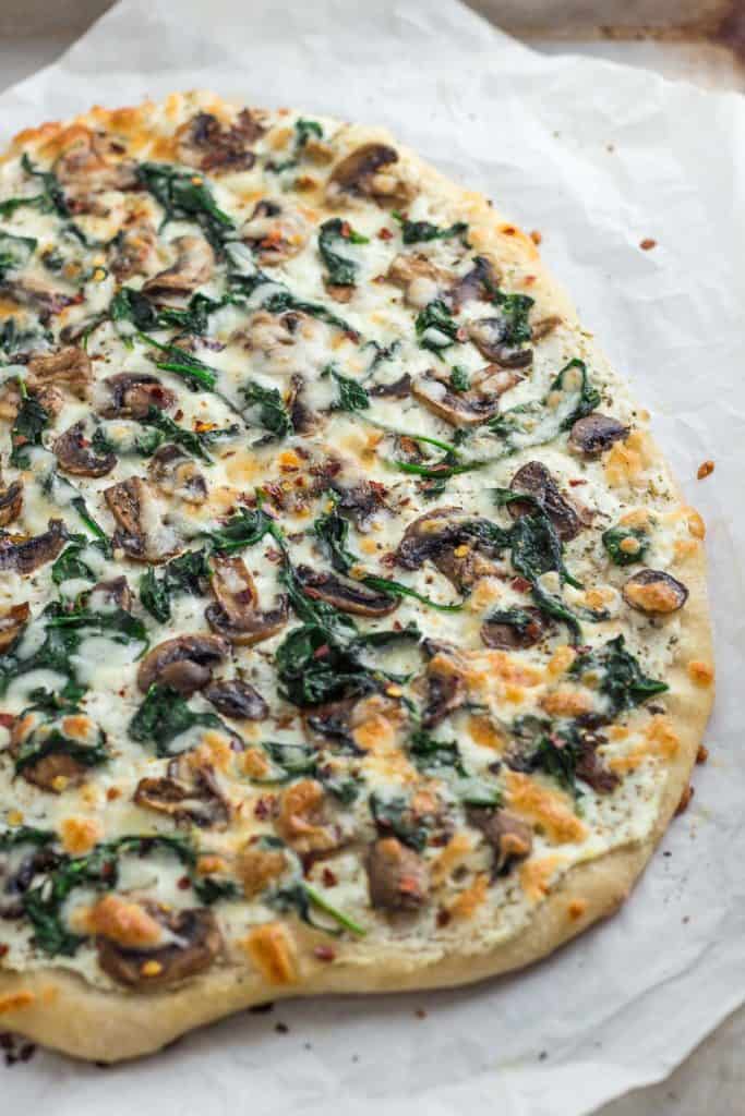 Whole mushroom spinach white pizza on the baking sheet after baking in the oven