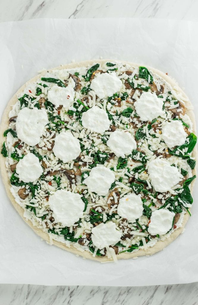 Whole white pizza with extra dollops of ricotta cheese on top, before baking in the oven