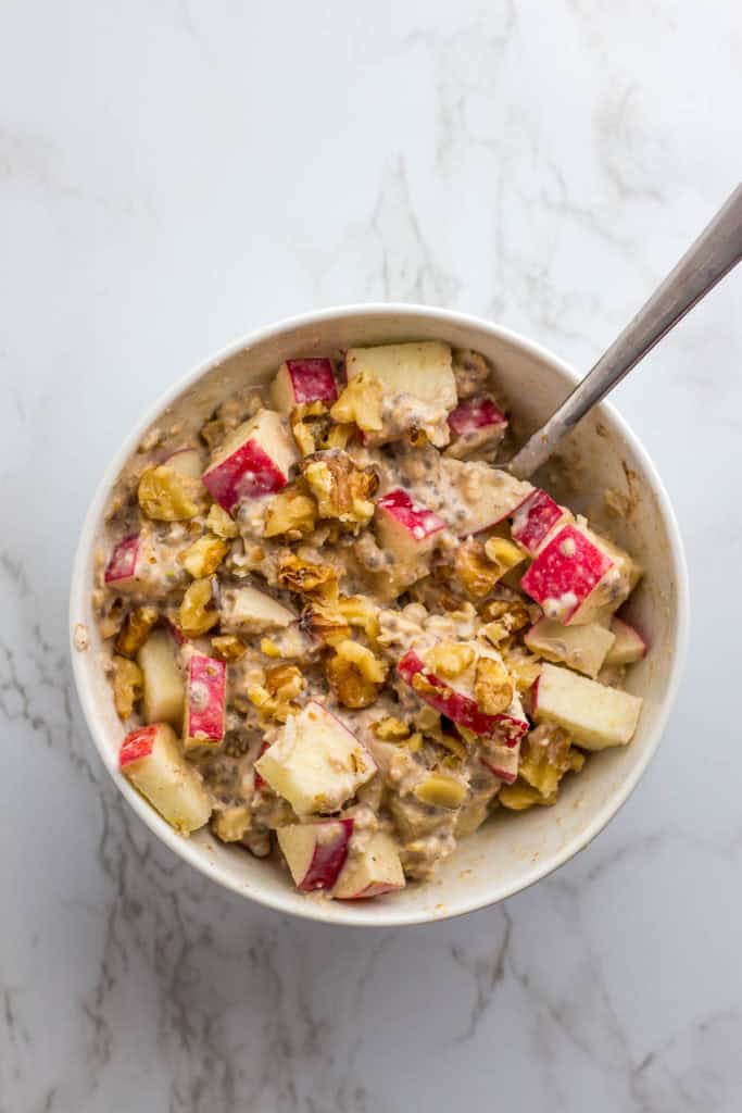 overnight oats in a white bowl with diced apple, cinnamon powder, and walnut pieces on top
