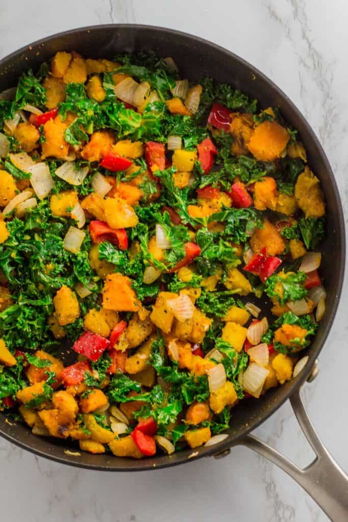 Cooked onion, red bell pepper, winter squash, and kale in the pan