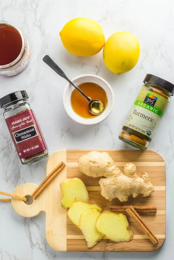 Fresh ginger root, cinnamon sticks, lemon, turmeric, and honey arranged on a marble surface, showing the main ingredients for homemade immune support tea.