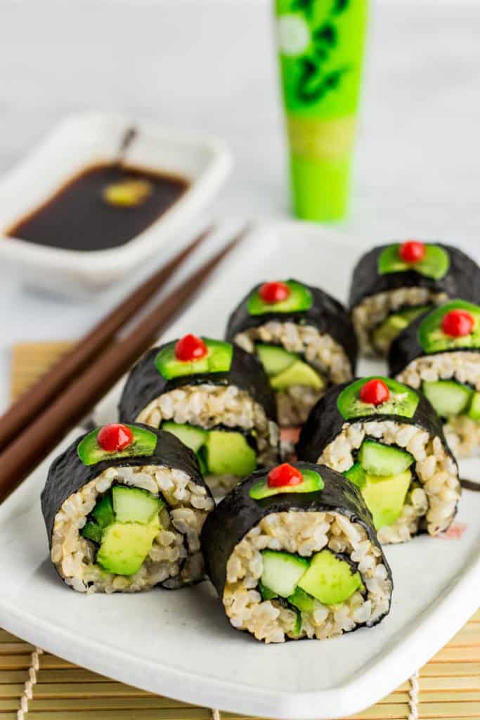 Close up shot of regular vegan green sushi roll (vegan uramaki). It is decorated with thin slice of jalapeno dotted with sriracha sauce on top of each roll.