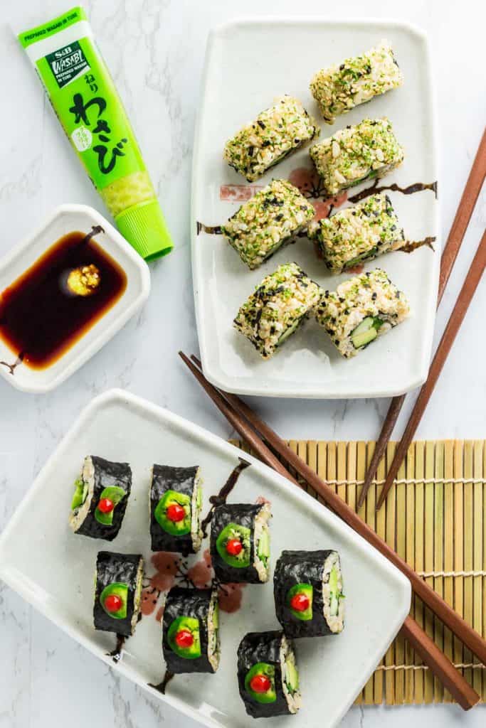 Over head shot of both inside out and regular vegan green sushi rolls. Two pair of chopsticks and soy sauce with wasabi paste is next to the rolls.