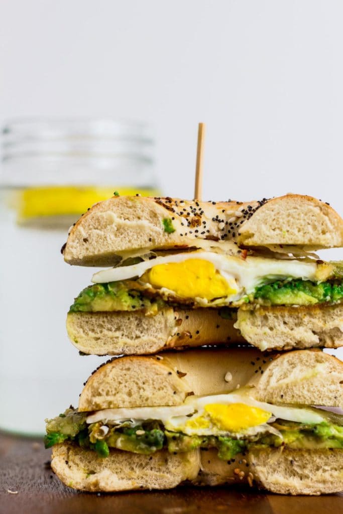 Cross cut of bagel sandwich, can see mashed avocado and fried egg