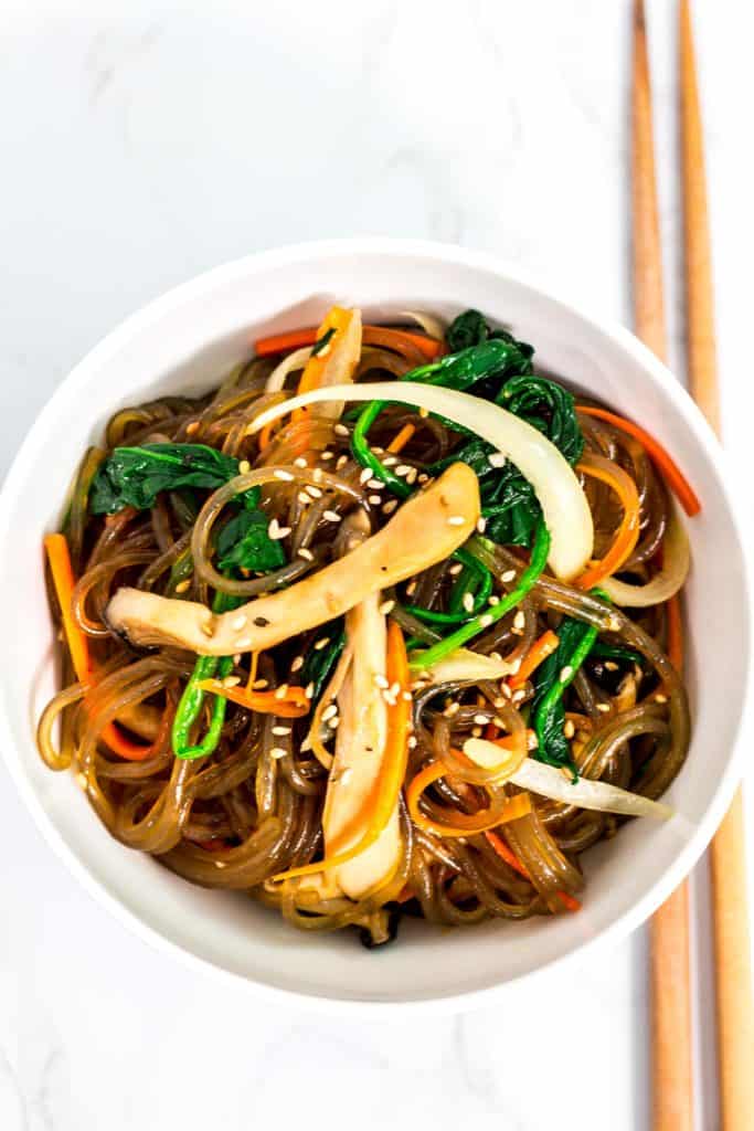 Overhead shot of Korean vegan japchae in a white bowl with chopsticks next to it