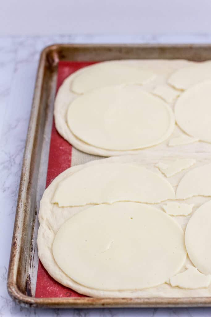 two pizza crusts layered with provolone cheese slices
