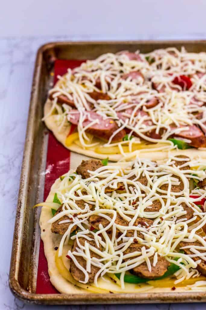 One chicken sausage pizza and one vegan sausage pizza before going in to the oven
