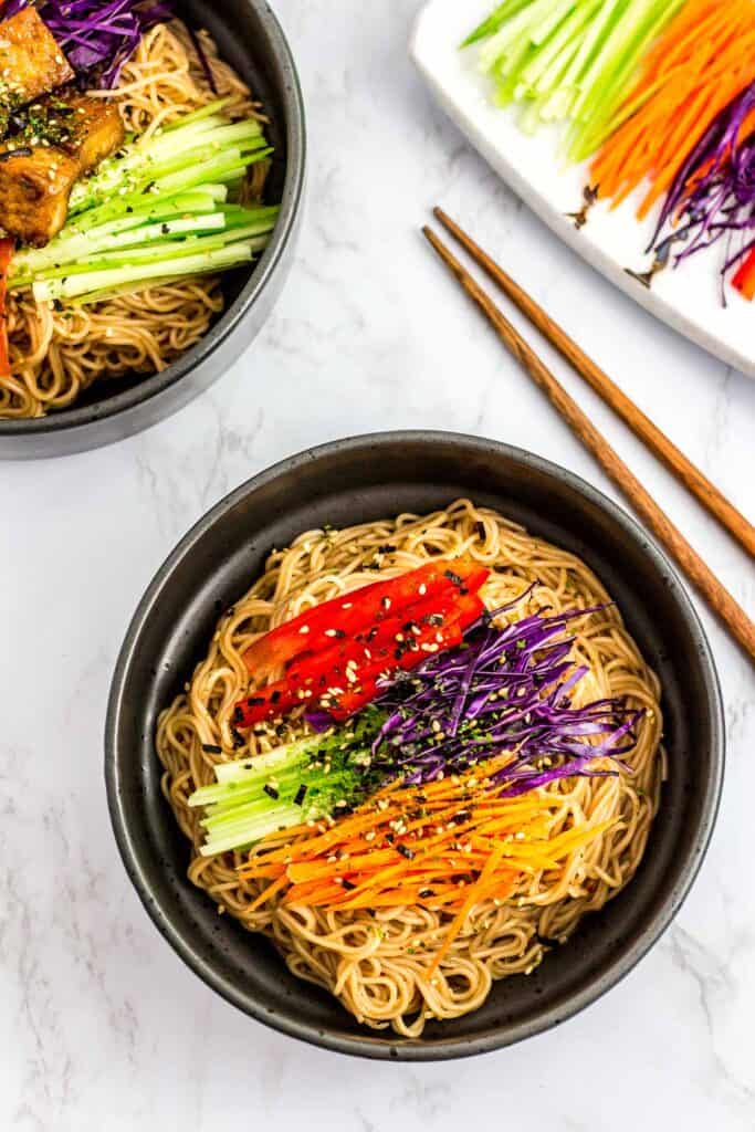 overhead shot of two bowls of Korean noodle salad with soy sauce with vegetables on the side