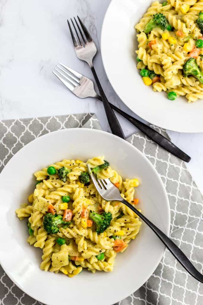 overhead shot of two plates of white veggie pasta with forks in the background