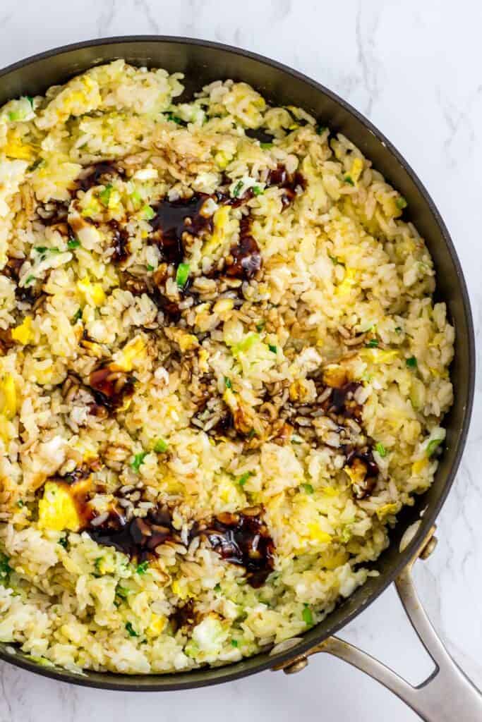 Mixture of fried egg, sauteed green onion and rice with vegetarian stir fry sauce on top, right before the sauce is mixed in