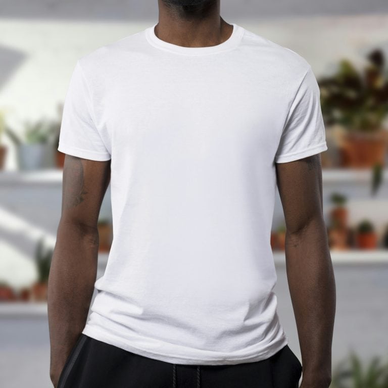 A man wearing a plain white t-shirt, standing in front of a blurred indoor background with potted plants.