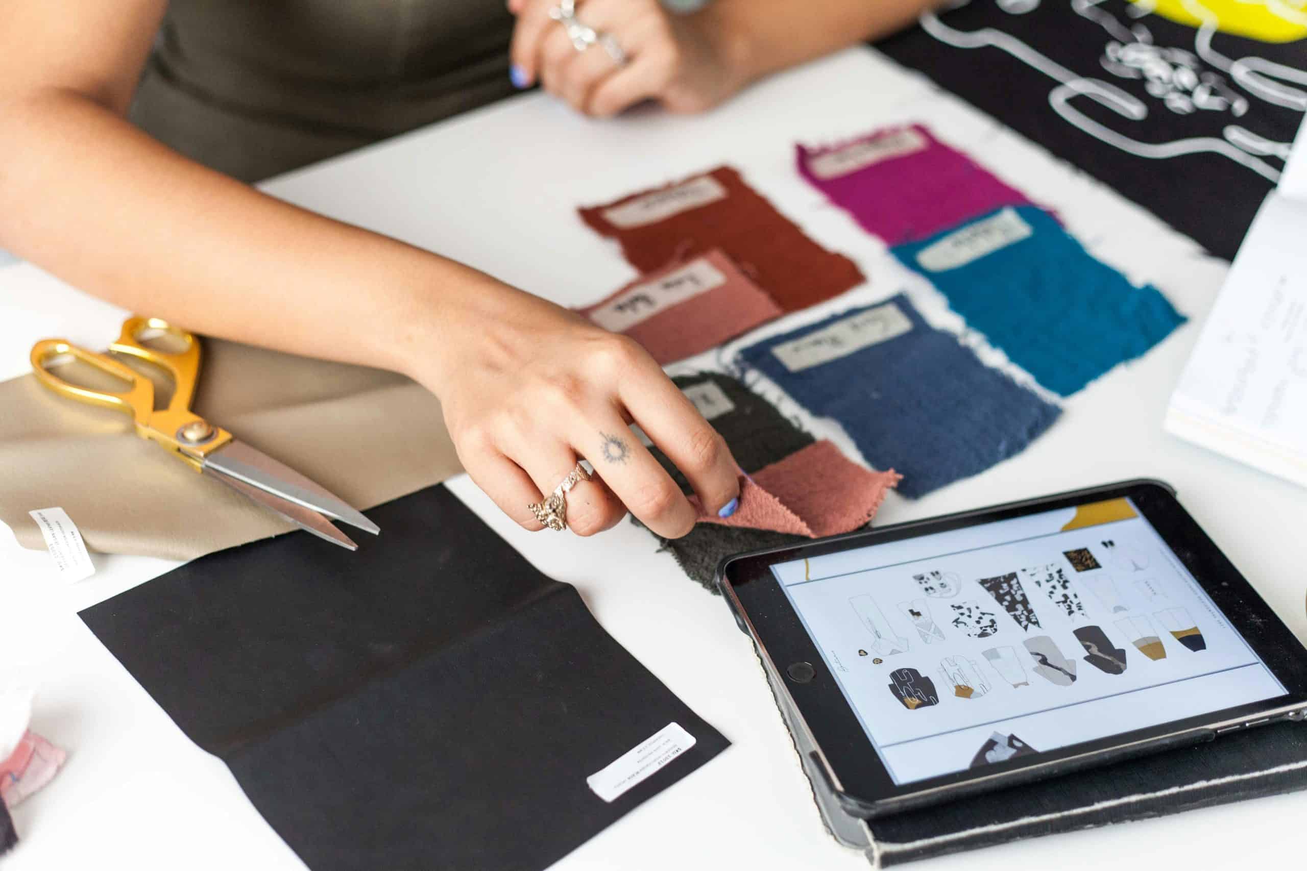 Un créateur de mode sélectionne des échantillons de tissus tout en utilisant une tablette comme référence.