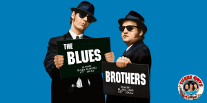 Two men in black suits and sunglasses holding movie-themed signs for "The Blues" and "Brothers".