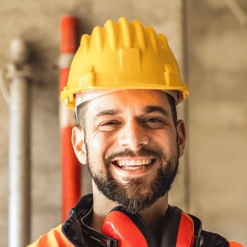 Smiling construction worker in a bright yellow hard hat and orange safety vest at a garage conversion site, symbolizing expert transformation services from garage to home library by A1 ADU Contractor.