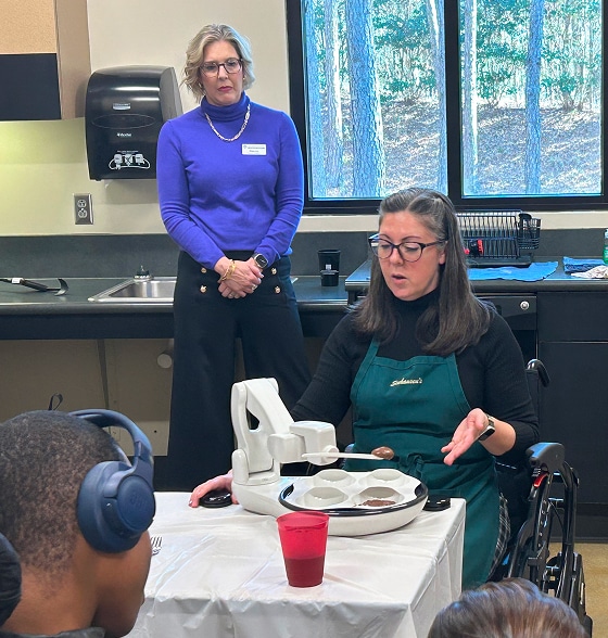 Jessica demonstrates a robotic feeding device to a group of people.