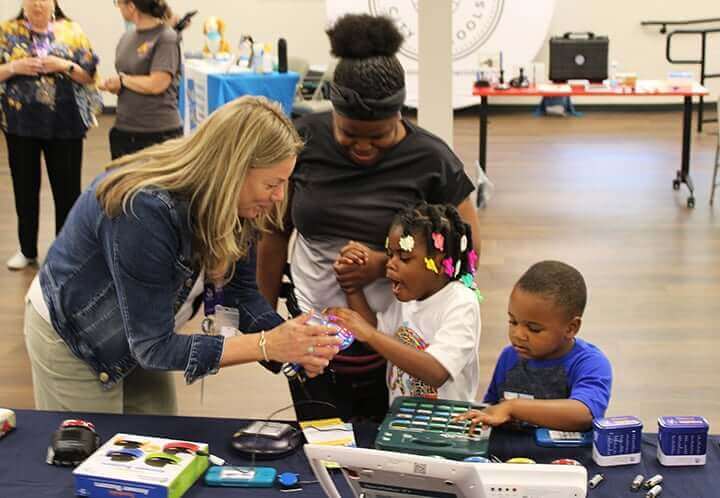 Lynn from APTAT shows two children a light-up object at a table with toys and devices