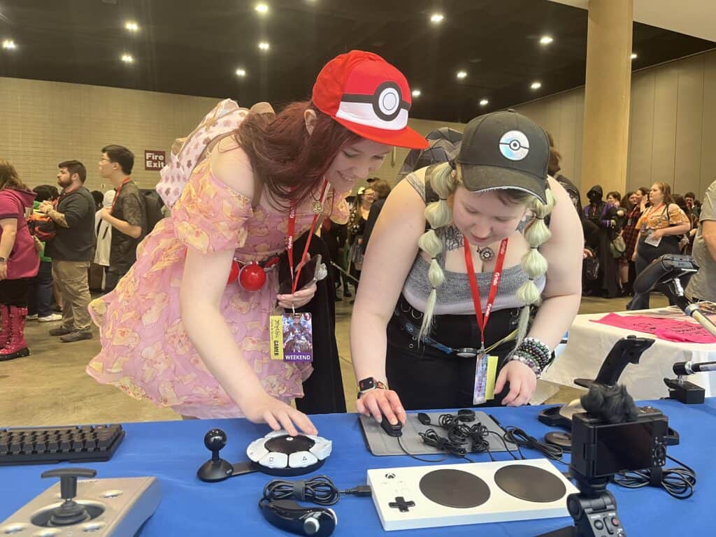 Two people in cosplay interact with adaptive gaming controllers at a convention