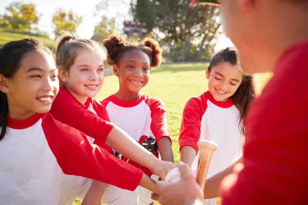 Schoolgirl baseball team in a team huddle with their coach