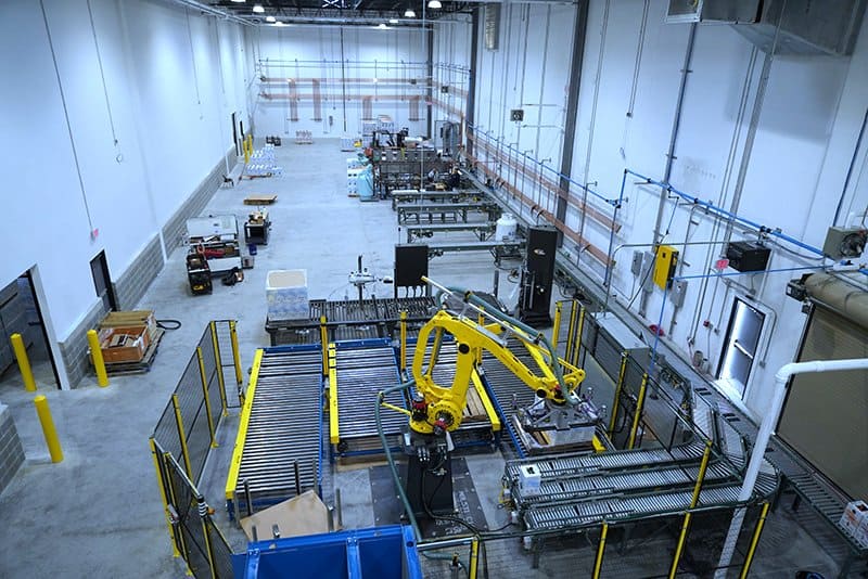 Robotic Carton Palletizing System including Fanuc M410iB/140H palletizing robot with indeed from Hytrol EZ Logic 24 volt zero pressure accumulation conveyor and Hytrol 138 ACC powered accumulating roller conveyor. Alba pallet dispenser, Alba CDLR pallet conveyor and Alba 3 strand chain transfer conveyor used to send palletized load to Wulftec WCA Smart stretch wrapper.