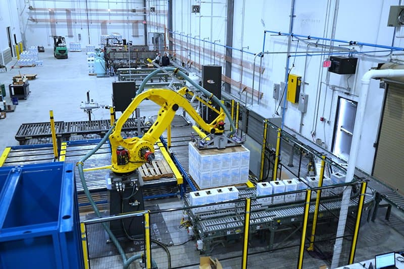Robotic Carton Palletizing System including Fanuc M410iB/140H palletizing robot with indeed from Hytrol EZ Logic 24 volt zero pressure accumulation conveyor and Hytrol 138 ACC powered accumulating roller conveyor. Alba pallet dispenser, Alba CDLR pallet conveyor and Alba 3 strand chain transfer conveyor used to send palletized load to Wulftec WCA Smart stretch wrapper.