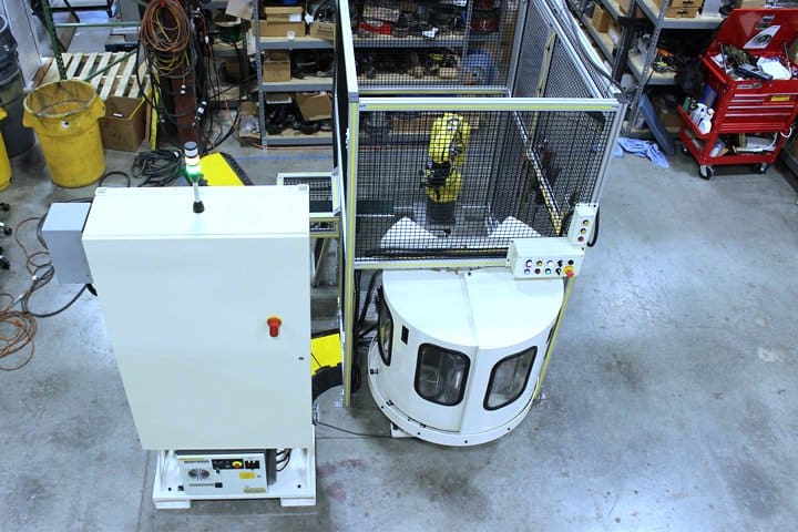 Automated manufacturing equipment in a factory setting with safety enclosure.