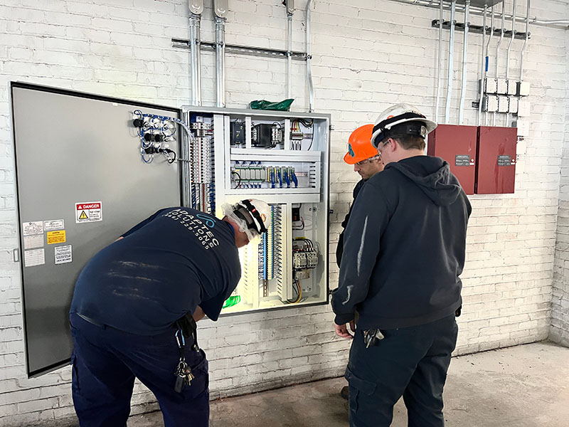 Electrical technicians inspecting control panel at industrial facility.