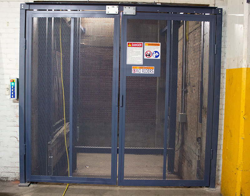 Elevator safety cage with warning signs and mesh doors for secure access.