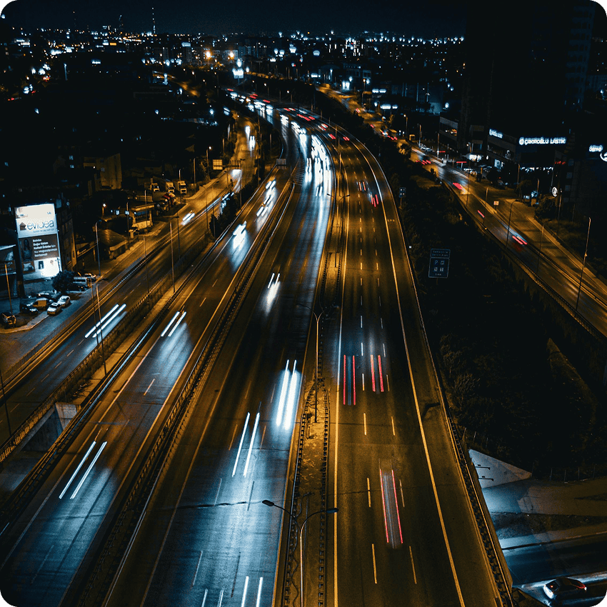 Night city traffic on highway with light trails, urban skyline at dusk.