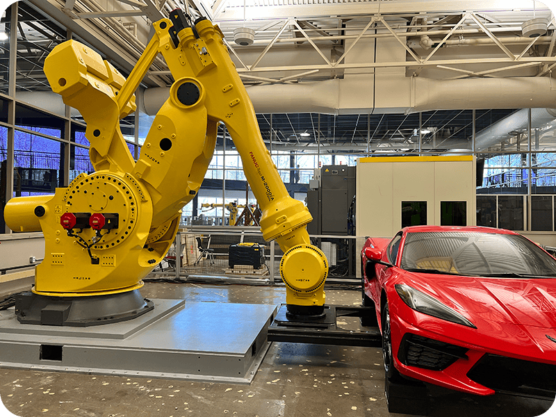 FANUC yellow robot holding red corvette