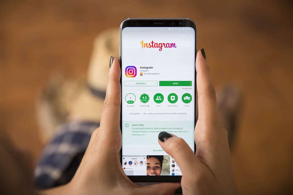 Close-up of a person holding a phone displaying the Instagram app page, representing social media advertising.