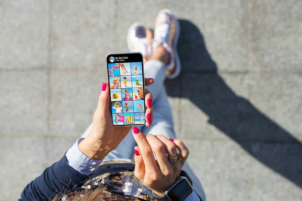 Person scrolling through a photo gallery on a smartphone outdoors, representing mobile content and social engagement.