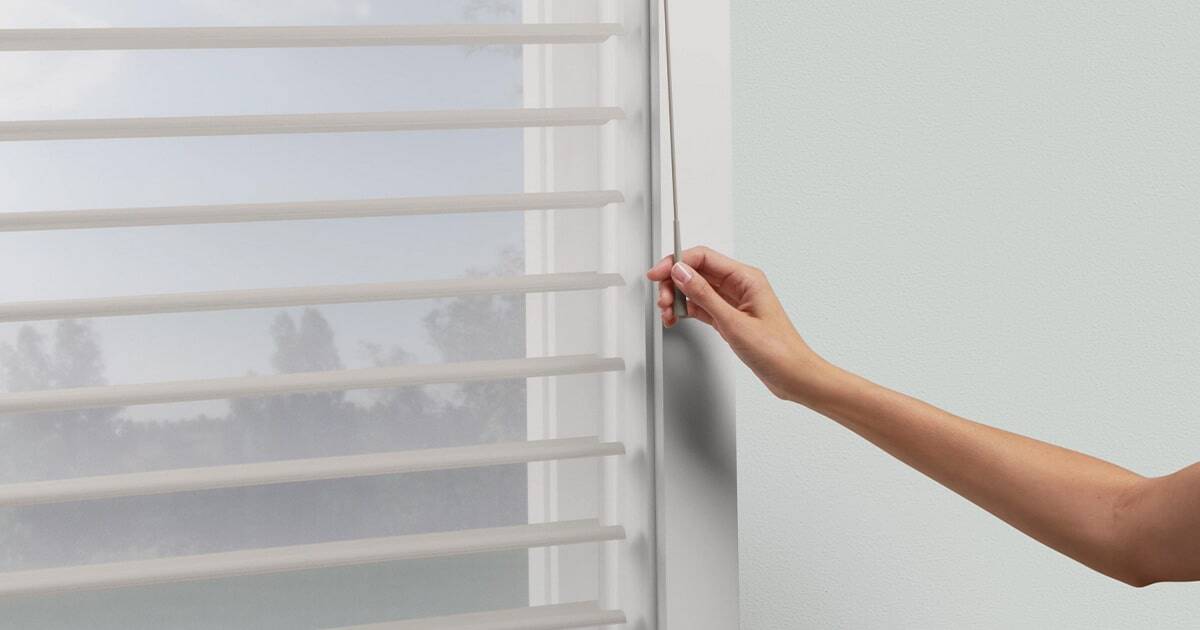 Light-filtering window blinds with a hand adjusting the tilt, ideal for enhancing privacy and controlling natural light in home interiors. Perfect for custom window treatments from Advance Blinds & Drapery.