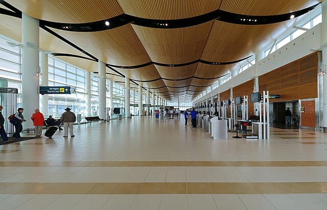 Airy airport terminal with large windows, modern wooden ceiling design, and check-in counters, showcasing bright, spacious, and well-lit travel environment.