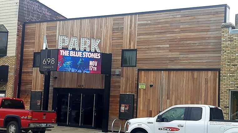 Black building facade with illuminated "PARK" sign and digital billboard advertising The Blue Stones concert.