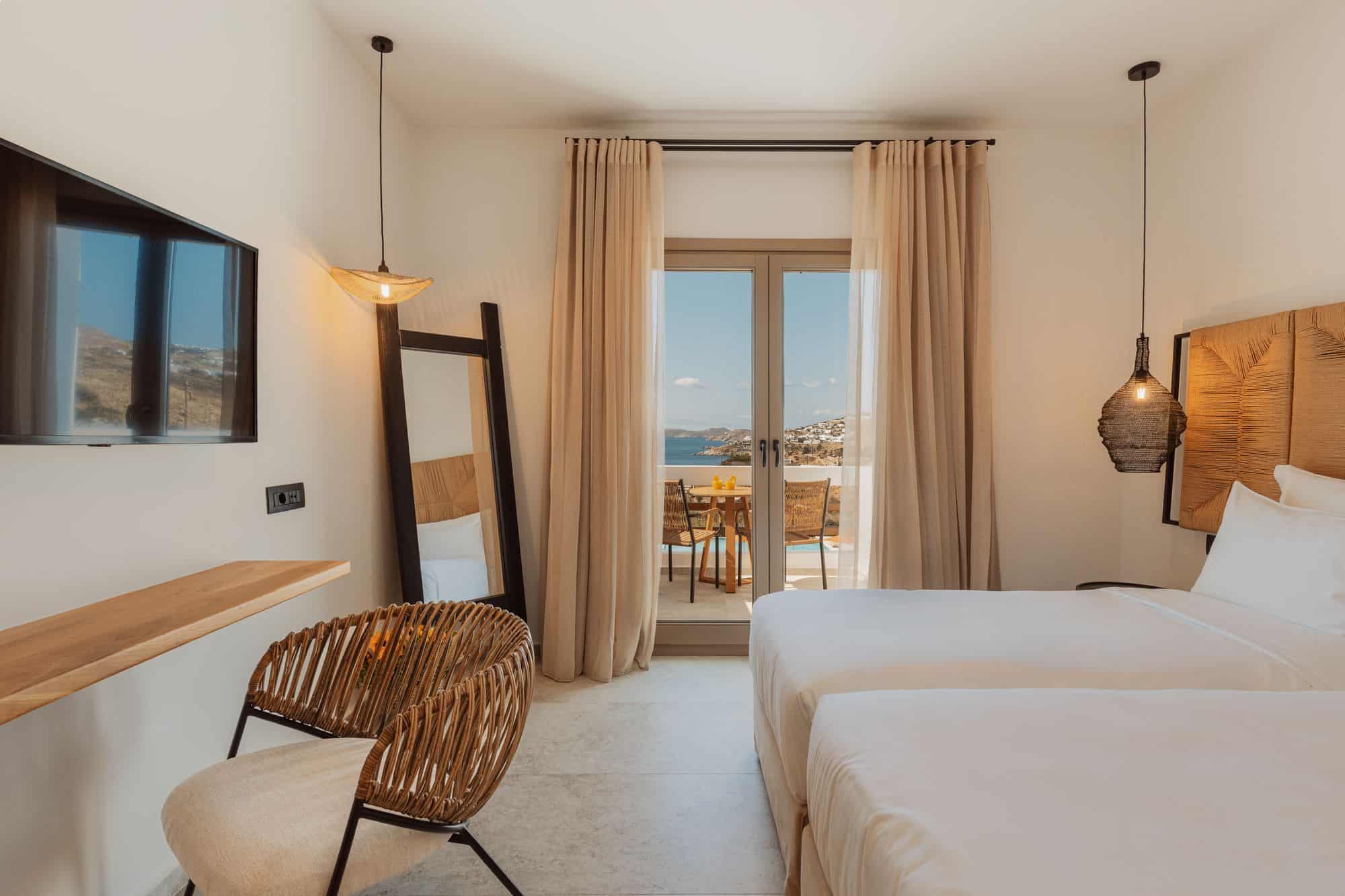Stylish Mykonos hotel room with sea view, two beds, modern decor, and terrace access.
